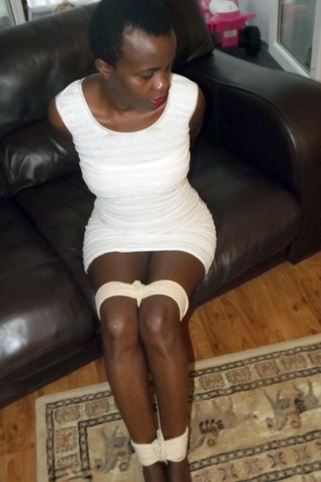 Black female is left tied and cleave gagged in a white dress on a leather sofa