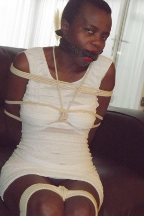 Black female is left tied and cleave gagged in a white dress on a leather sofa