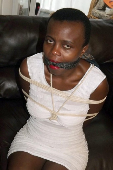 Black female is left tied and cleave gagged in a white dress on a leather sofa