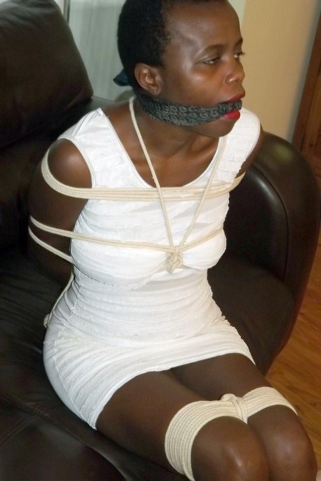 Black female is left tied and cleave gagged in a white dress on a leather sofa
