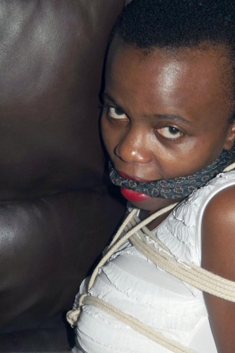 Black female is left tied and cleave gagged in a white dress on a leather sofa