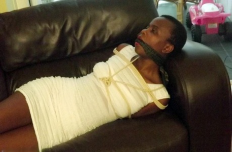 Black female is left tied and cleave gagged in a white dress on a leather sofa
