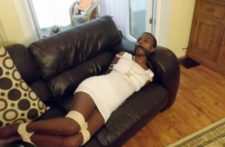 Black female is left tied and cleave gagged in a white dress on a leather sofa