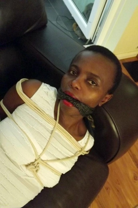 Black female is left tied and cleave gagged in a white dress on a leather sofa