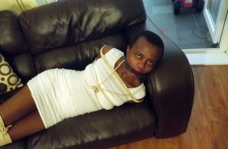 Black female is left tied and cleave gagged in a white dress on a leather sofa