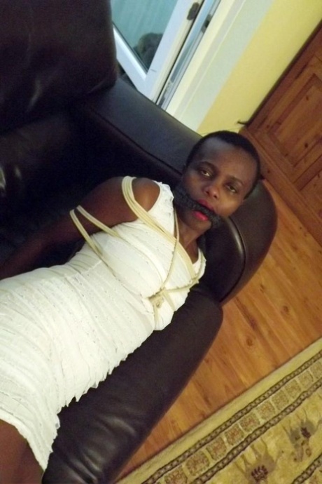 Black female is left tied and cleave gagged in a white dress on a leather sofa